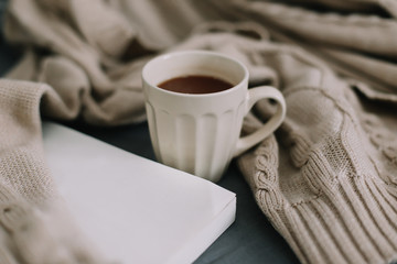 Wool beige sweater, warm knitted plaid, a book and coffee cup. Breakfast in bed. Sweet home. flat lay, still life
