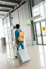 back view of african american man walking with suitcase and backpack in airport