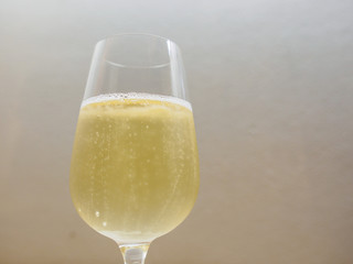 Wide closeup detail of a glass of Champagne with fizzy bubbles from the bottom. White shallow focus background. Sparkling wine and celebration.