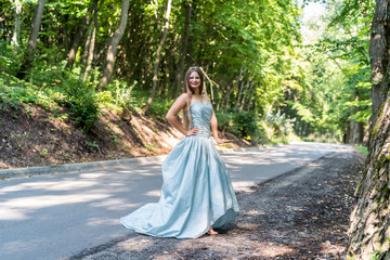 Obraz na płótnie Canvas Girl in dress on the summer road between trees