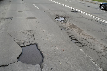 Fototapeta premium Poor condition of the road surface. Spring season. Hole in the asphalt, risk of movement by car, bad asphalt, dangerous road, potholes in asphalt. Kiev,Ukraine