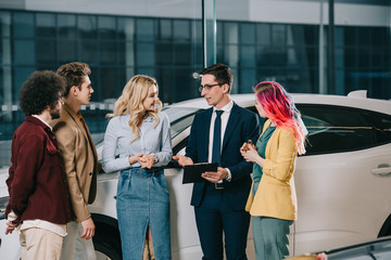Fototapeta premium handsome car dealer holding clipboard and taking with group of friends