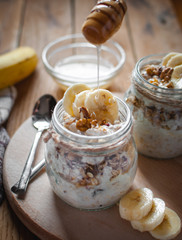 Close-up of homemade banana oats in a glass jar with honey dripping, on wooden background
