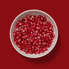Closeup of pomegranate beans in a white porcelain bowl isolated on red background	