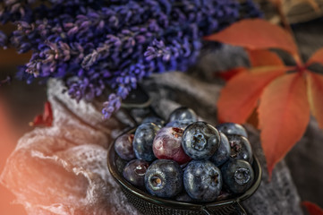 Blue berries blueberries in wicker white basket with autumn leaves in a rustic style. Close-up.