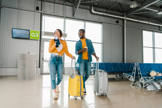smiling african american couple walking together in airport with travel bags