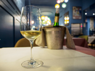 Wide closeup of a glass of Alsatian white wine as an aperitif at a romantic restaurant dinner. Shallow focus, bucket and chilled bottle on table in background. Colmar, France. Travel and cuisine.
