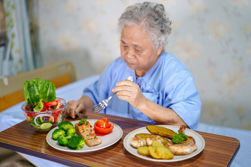 Asian senior or elderly old lady woman patient eating breakfast healthy food with hope and happy while sitting and hungry on bed in hospital.