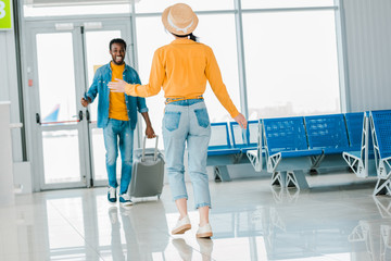 selective focus of happy african american man with suitcase walking towards girlfriend in airport