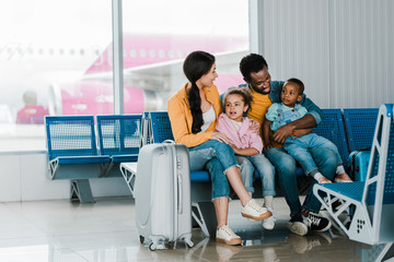 Fototapeta premium smiling african american family with baggage and kids sitting in airport