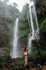Unrecognizable Woman in bikini enjoying waterfall in jungle