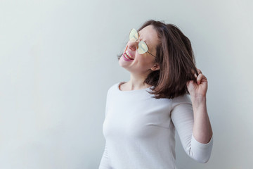 Fototapeta premium Simple studio portrait of hipster fashion smiling short-haired brunette girl in trendy yelow sunglasses isolated on white background. Fun positive young smart woman in glasses having fun smiling