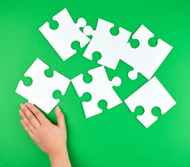 female hand puts empty white big puzzles on a green background