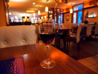 Wide closeup of a glass of red Bordeaux wine at a warmly lit, romantic restaurant dinner. Shallow focus. Strasbourg France. Travel and cuisine.