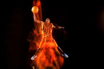 Play in fire. African-american young basketball player of red team in action and neon lights over...