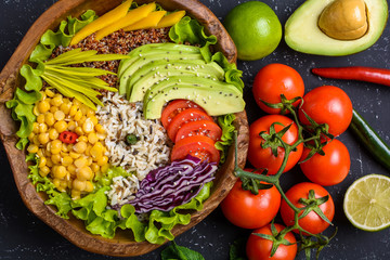 Healthy vegan superfood bowl with quinoa, wild rice, chickpea, tomatoes, avocado, greens, cabbage, lettuce on black stone background top view. Food and health