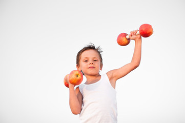 one little caucasian boy in white tank top lifting apple fruit dumbbells on white background