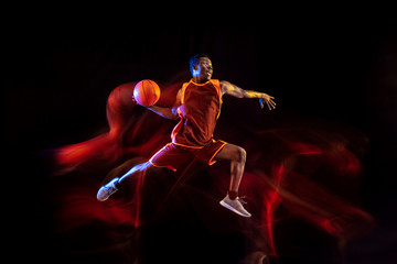 See the target. African-american young basketball player of red team in action and neon lights over dark studio background. Concept of sport, movement, energy and dynamic, healthy lifestyle.