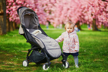 One year old girl standing next to her pushchair in park