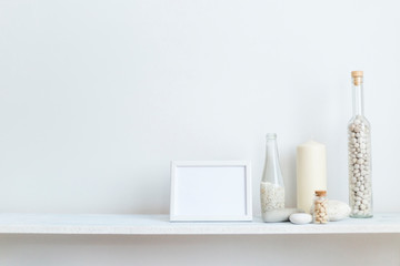 Shelf against white wall with decorative candle, glass and rocks.