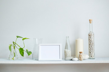 Obraz na płótnie Canvas Shelf against white wall with decorative candle, glass and rocks. Plant cuttings in glass.