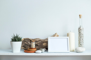 Shelf against white wall with decorative candle, glass, wood and rocks. Home plant in pot.