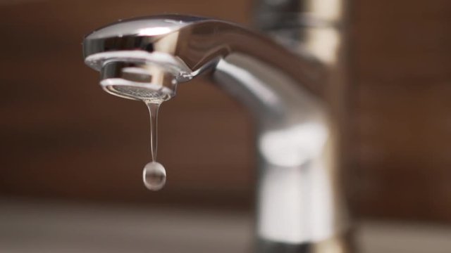 Panoramic shot of dripping tap in bathroom. Water waste, slow motion