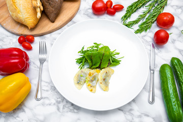 Dumplings, filled with cabbage. vegetable dumplings. Dumplings with potatoes in plate on white background. Ingredients for dumplings with cabbage, potatoes, tomato, cucumber, lettuce, pepper. Top vie