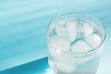 Close up of pure water with ice in transparent glass and sun glare on blue  background.