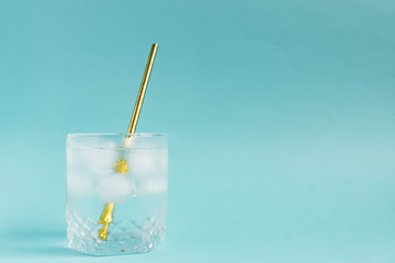 Close up of pure water with ice and paper straw in transparent glass and sun glare on blue ...