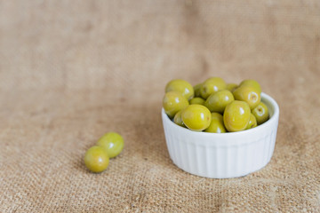  fresh marinated green olives in white ceramic bowl on  burlap cloth background