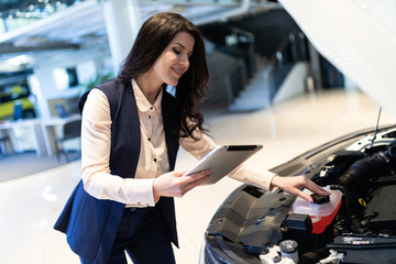 Beautiful sale-manger inspect new car with help of tablet in dealership center