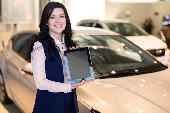Stylish insurance agent standing near the car and holding a tablet