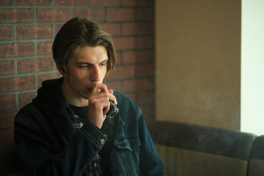 Vape teenager. Portrait of young handsome guy smoking an electronic cigarette in the bar. Bad habit that is harmful to health. Vaping activity.