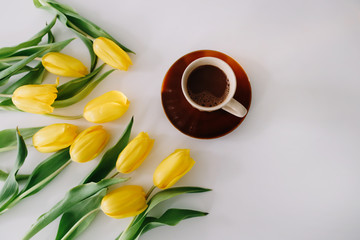 A coffee cup in a frame of tulips on white background. Flat lay, top view. Concept of holiday, birthday, Easter, March 8