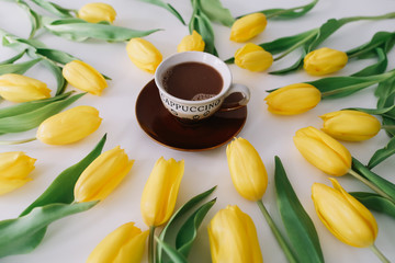 A coffee cup in a frame of tulips on white background. Flat lay, top view. Concept of holiday, birthday, Easter, March 8