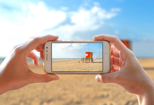 Photo camera of a smartphone. Young woman takes a photo of the beach in a sunny day of summer. 