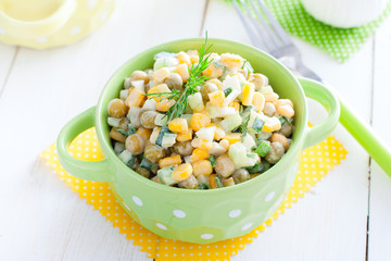 Bright salad with peas and corn in colored dishes on a white table, horizontal