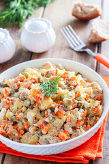 Russian salad in spanish with canned tuna on a white plate on a wooden table, horizontal