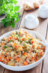Russian salad in spanish with canned tuna on a white plate on a wooden table, horizontal