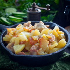 Fried potatoes with chicken on a cast-iron black pan, square