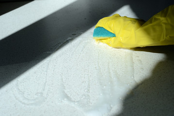Hand in rubber glove washing surface lit by the sun. Spring cleaning