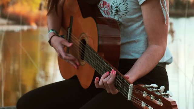 Young woman playing guitar near water