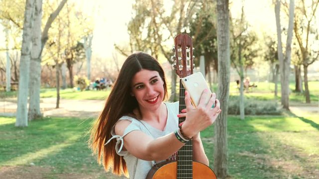 Smiling female guitarist taking selfie in park