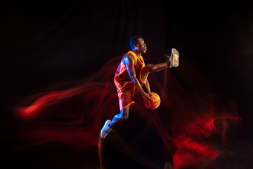 Higher and stronger. African-american young basketball player of red team in action and neon lights...