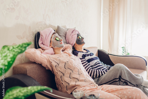 Mother and her adult daughter relaxing with facial masks and cucumbers applied. Women chilling and having fun at home