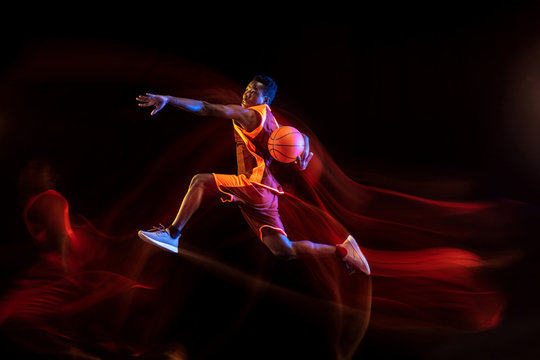 Choosing the right way. African-american young basketball player of red team in action and neon lights over dark studio background. Concept of sport, movement, energy and dynamic, healthy lifestyle.