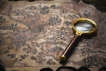 Old map and a magnifying glass on a adventurer table background. Treasure hunt concept.