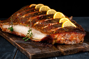 Baked Halibut fish with lemon on wooden board on dark background, hot smoked seafood