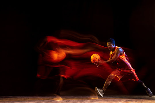 Melting track of fire. African-american young basketball player of red team in action and neon lights over dark studio background. Concept of sport, movement, energy and dynamic, healthy lifestyle.